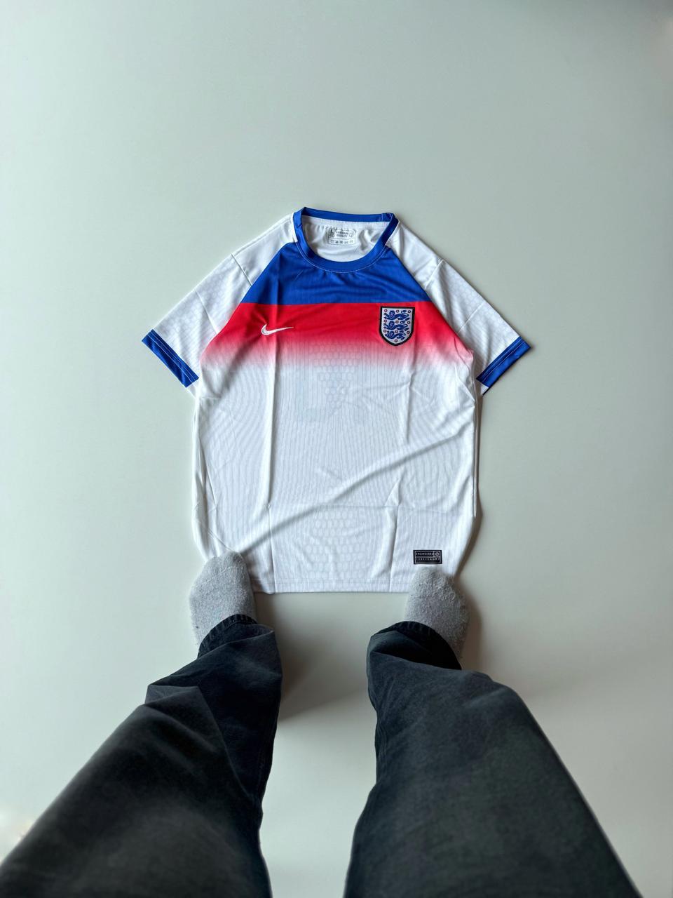 Front view flat lay of the England 2024 home style mashup football jersey featuring a red and blue gradient chest panel block and premium embroidered Three Lions crest at vamstore India.