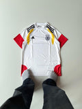Front view flat lay of the Germany 2024 home jersey featuring the iconic white template and vibrant black, red, and gold gradient eagle-wing shoulder graphics at vamstore India.