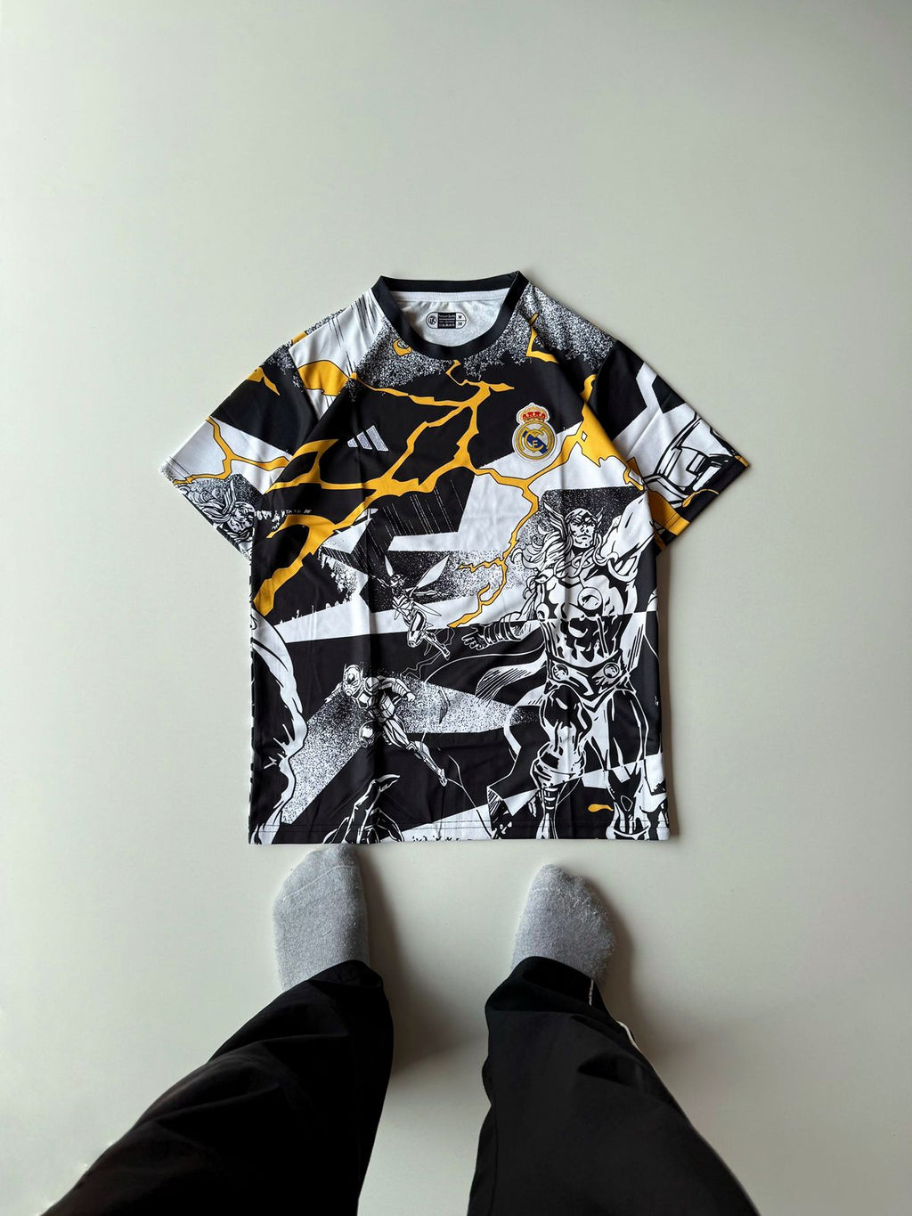 Front view flat lay of the Real Madrid 2024 2025 special edition Marvel Avengers jersey featuring a black and white comic book collage pattern with yellow lightning accents at vamstore India.