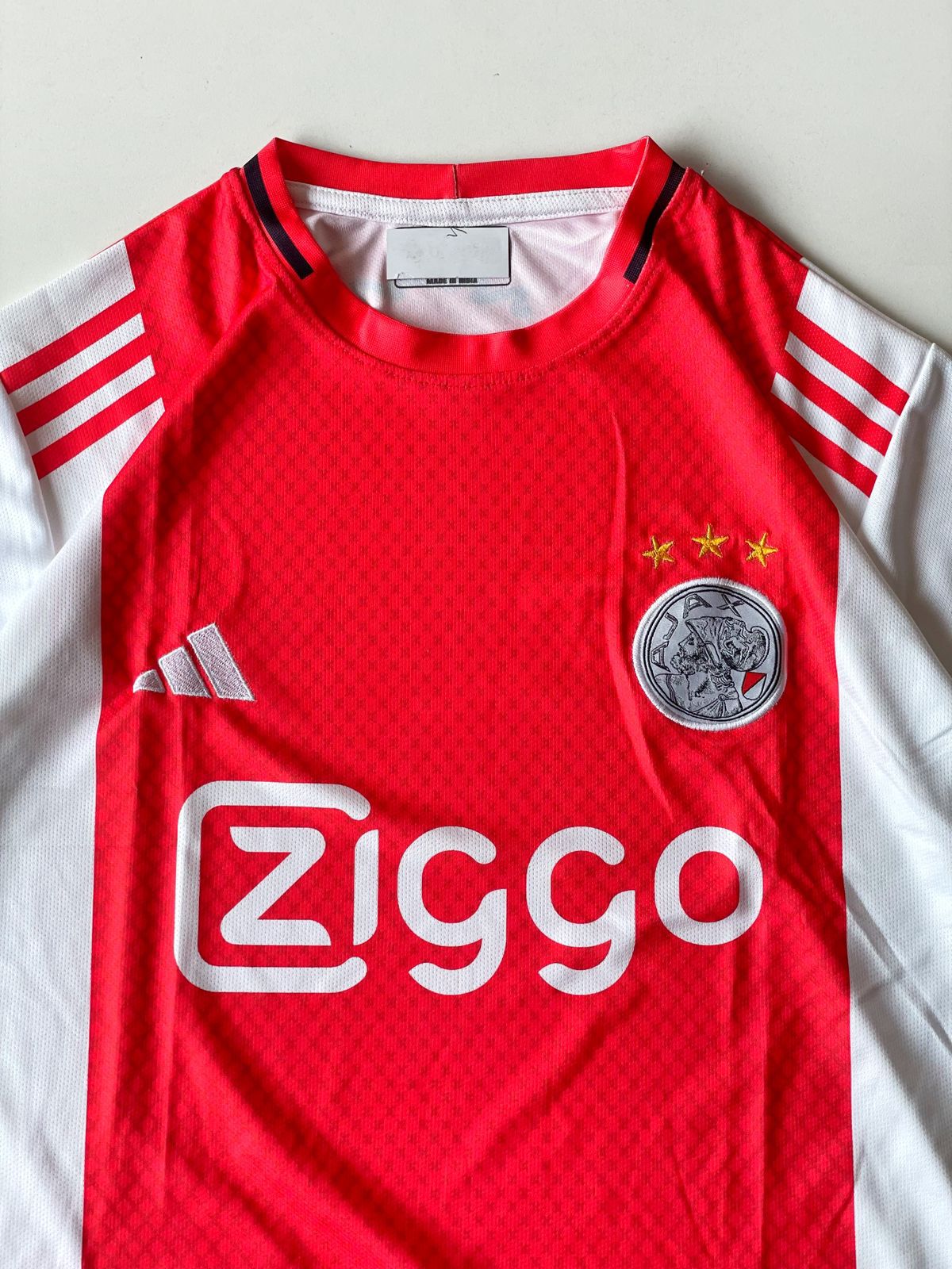 Close-up detail of the Ajax Amsterdam 2024 2025 home kit showing high-density stitched club emblem with three championship stars at vamstore India.